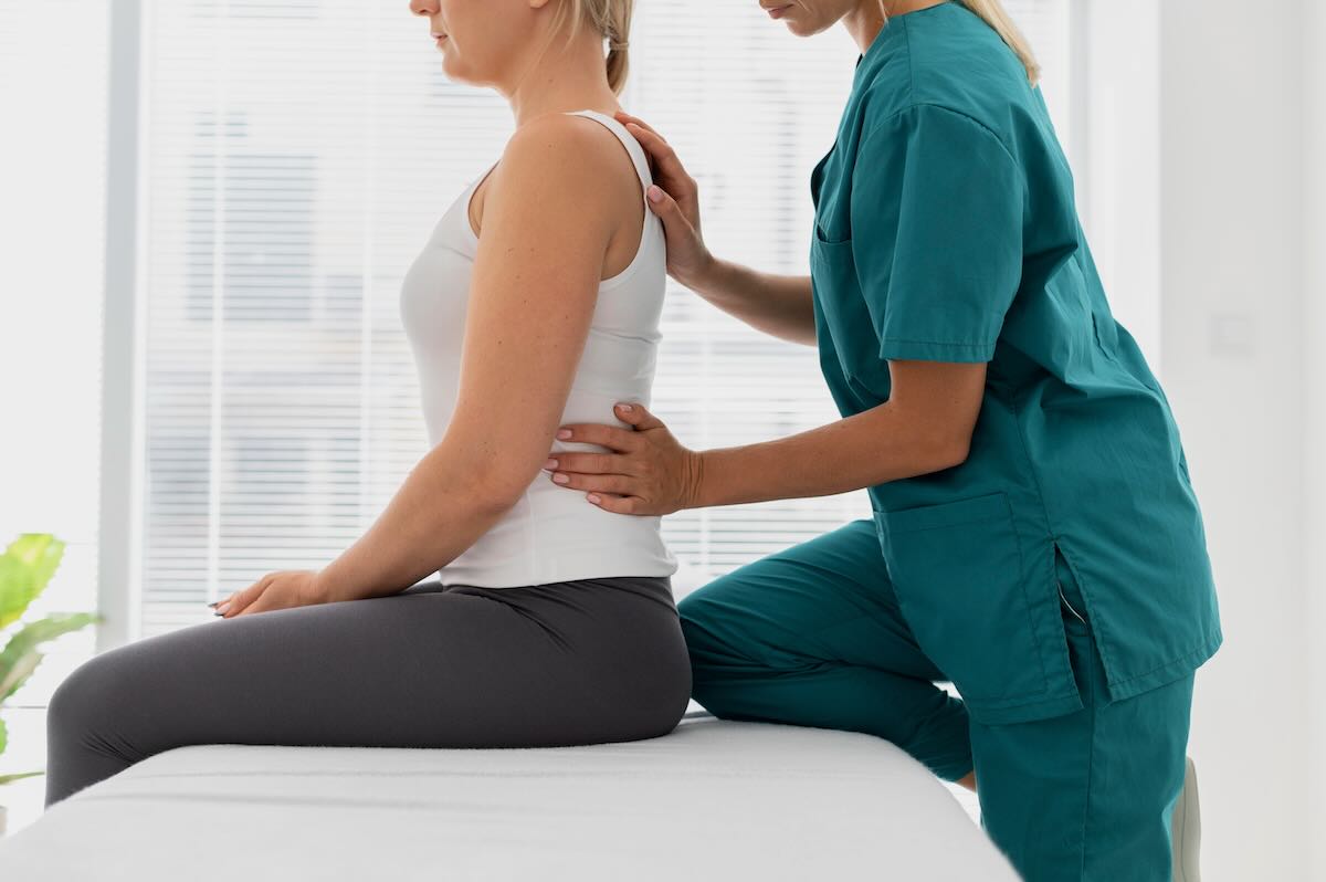 Médico de Fermaz Salud realiza una palpación y ajuste manual en la espalda baja de una paciente con camiseta blanca, quien está sentada erguida en una camilla clínica, mostrando una sesión de tratamiento para problemas de espalda en Madrid.